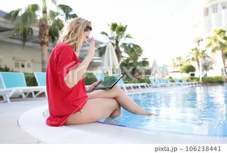 Woman happily greets with hand business partners on tablet while sitting in pool 106238441