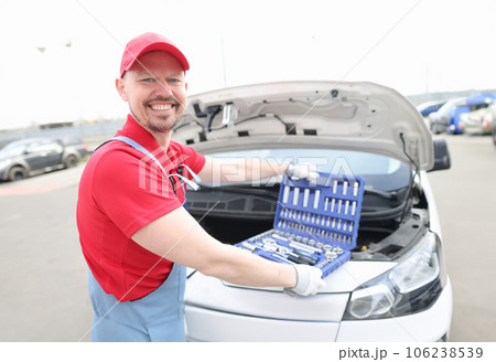 Portrait of young smiling car repairman with set of tools on hood of car Portrait of young smiling car repairman with set of tools on hood of car 106238539