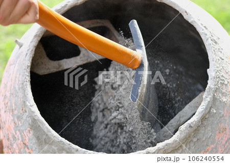Construction site. Adding lime, sand and stones to rotating cement mixer. Builder working with shovel during concrete solution mortar preparation. Bricklayer job machine equipment. Cement slurry 106240554