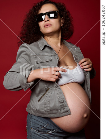 Pregnant woman, expectant mother wearing trendy sunglasses, isolated over red studio background. Childbearing. Pregnancy Pregnant woman, expectant mother wearing trendy sunglasses, isolated over red studio background. Childbearing. Pregnancy 106242067