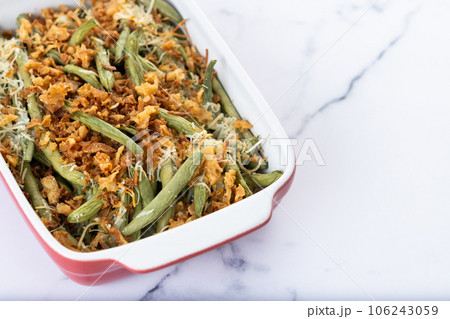 A traditional green bean casserole topped with French Fried Onions and cream of mushroom on white marble. Close up A traditional green bean casserole topped with French Fried Onions and cream of mushroom on white marble. Close up 106243059