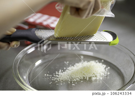 グリュイエールチーズをグレーターですり下ろす女性の手元 106243334