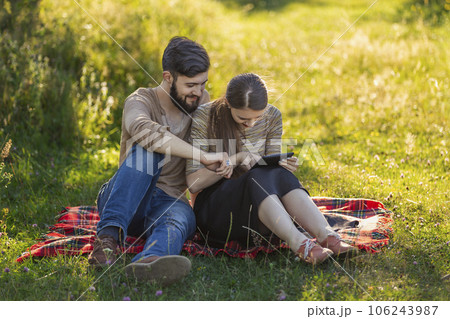 Young couple sitting in nature and looking at a tablet Young couple sitting in nature and looking at a tablet 106243987