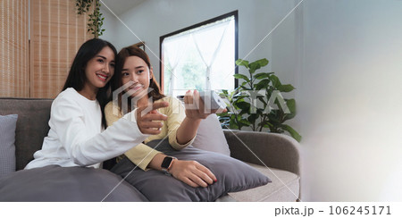 Asian young woman homosexual lesbian couple put on sweater sitting on sofa to watching cinema in living room at home 106245171