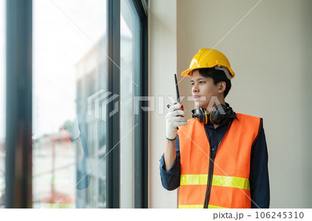 Asian male engineer standing at construction site and communicating with walkie talkie Asian male engineer standing at construction site and communicating with walkie talkie 106245310