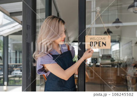 Portrait of a happy cafe owner standing at cafes entrance. Portrait of mature business in her coffee shop. Happy woman owner showing open sign in her small business shop Portrait of a happy cafe owner standing at cafes entrance. Portrait of mature business in her coffee shop. Happy woman owner showing open sign in her small business shop 106245502