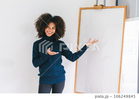 Studio portrait of Beautiful young African American woman smiling at camera pointing her finger at whiteboard. Studio portrait of Beautiful young African American woman smiling at camera pointing her finger at whiteboard. 106249845