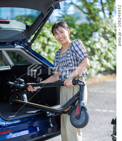 旅行先の駐車場で電動キックボードを車のトランクに収納する若くて可愛い女性 旅行先の駐車場で電動キックボードを車のトランクに収納する若くて可愛い女性 106249952
