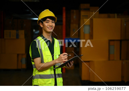 Male worker wearing safety hardhat and vest checking quantity of storage product on shelf in a large warehouse Male worker wearing safety hardhat and vest checking quantity of storage product on shelf in a large warehouse 106259077