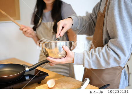Young man wearing apron mixing ingredients in bowl, preparing breakfast with girlfriend in kitchen 106259131