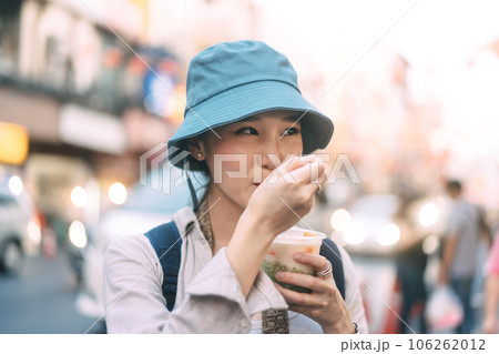 Closeup young adult asian foodie woman backpack traveller eating asia dessert street food Closeup young adult asian foodie woman backpack traveller eating asia dessert street food 106262012