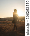 夕日の中、草原で流離うトレンチコートを着た女性 106262550