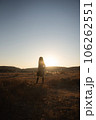 夕日の中、草原で流離うトレンチコートを着た女性 106262551
