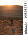 夕日の草千里でトレンチコートの女性が立ってる 106262554
