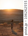 夕日の草千里でトレンチコートの女性が立ってる 106262555