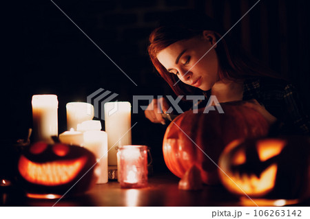 Young woman making Halloween pumpkin Jack-o-lantern with candles in dark. Female hands cutting pumpkins with knife 106263142