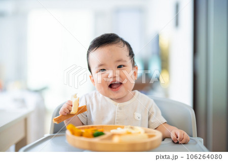 離乳食後期でをつかみ食べをしてご機嫌な生後9か月の赤ちゃん 106264080