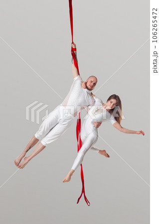 Beautiful girl and an athletic man in a white sport suits are performing an acrobatic elements in a studio. 106265472