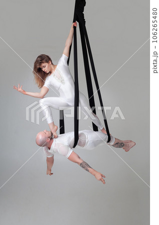 Beautiful girl and an athletic man in a white sport suits are performing an acrobatic elements in a studio. Beautiful girl and an athletic man in a white sport suits are performing an acrobatic elements in a studio. 106265480