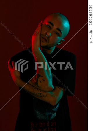 Studio shot of a young tattoed bald man posing against a red background. 90s style. Studio shot of a young tattoed bald man posing against a red background. 90s style. 106265556