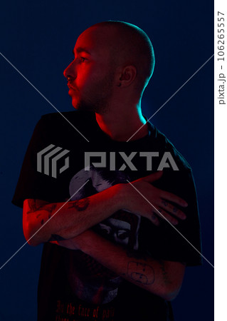Studio shot of a young tattoed bald man posing against a blue background. 90s style. Studio shot of a young tattoed bald man posing against a blue background. 90s style. 106265557