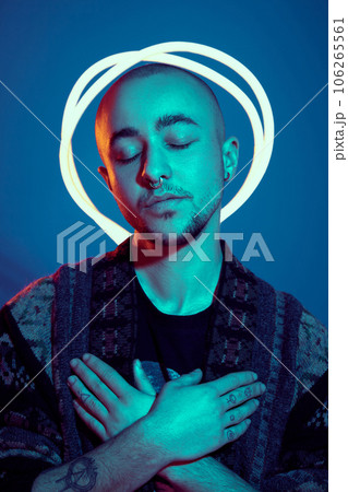 Studio shot of a young tattoed bald man posing against a blue background. 90s style. Studio shot of a young tattoed bald man posing against a blue background. 90s style. 106265561
