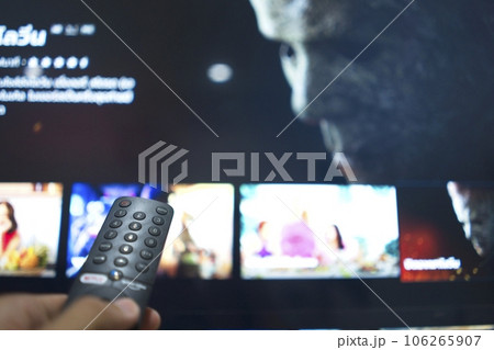 Hand with TV remote control, switching TV series from streaming service platform. The new way of enjoying entertainment at home. Hand with TV remote control, switching TV series from streaming service platform. The new way of enjoying entertainment at home. 106265907