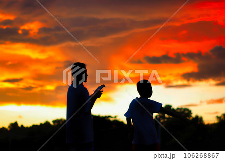 Silhouette of a boys piloting a drone on A Rural Setting on sunset 106268867