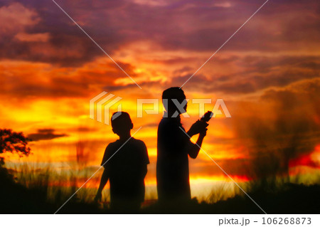 Silhouette of a boys piloting a drone on A Rural Setting on sunset 106268873