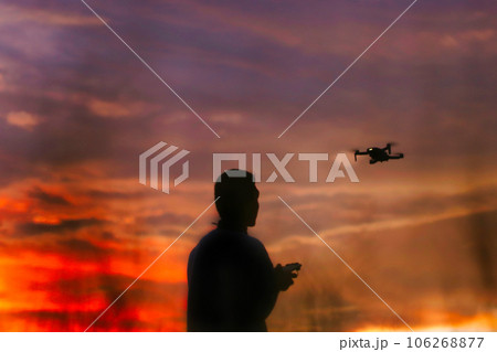 Silhouette of a boys piloting a drone on A Rural Setting on sunset 106268877