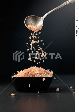 Pink salt is poured into a small black bowl. Pink salt is poured into a small black bowl. 106269508