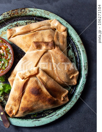 Tipical baked empanadas de pino with pebre sauce on vintage try, black stone background. Traditional chilean food for independence day party 106271584
