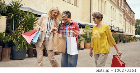 Mature women ladies is walking outdoors after shopping and bragging about successful purchases Mature women ladies is walking outdoors after shopping and bragging about successful purchases 106273361