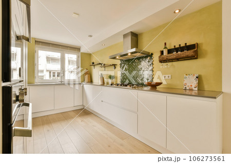 a kitchen with white cabinets and wood flooring in the middle part of the room, there is an oven on the wall a kitchen with white cabinets and wood flooring in the middle part of the room, there is an oven on the wall 106273561