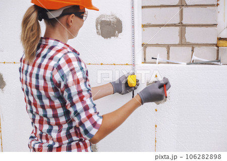 Insulation of the house with polyfoam. The worker is checking with the construction level the accuracy of the installation of polystyrene board on the facade. 106282898