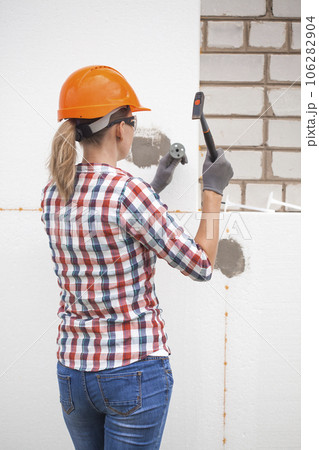 Insulation of the house with polyfoam. The worker is checking with the construction level the accuracy of the installation of polystyrene board on the facade. 106282904