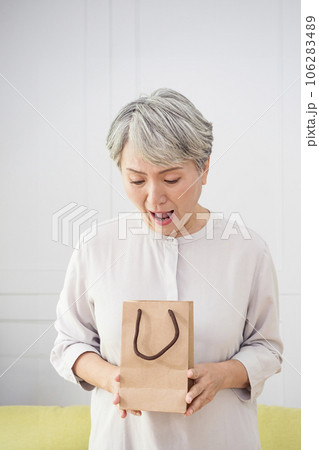 Portrait of an elderly Asian woman receives gift boxes, smiling and looking down while standing in a living room at home. Portrait of an elderly Asian woman receives gift boxes, smiling and looking down while standing in a living room at home. 106283489