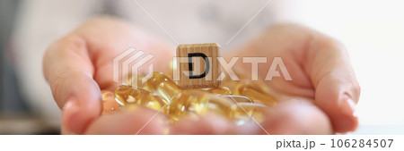 Human hands holding pile of vitamin D capsules with wooden cube with D symbol close up. 106284507