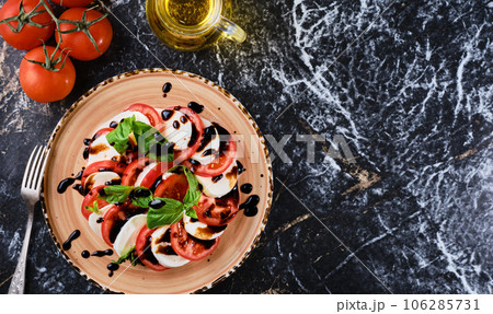 Tomatoes and mazzarella, Italian Caprese salad with tomatoes, mozzarella cheese, basil balsamic vinegar and olive oil. Dark marble background, top view, Vegetarian dish Tomatoes and mazzarella, Italian Caprese salad with tomatoes, mozzarella cheese, basil balsamic vinegar and olive oil. Dark marble background, top view, Vegetarian dish 106285731