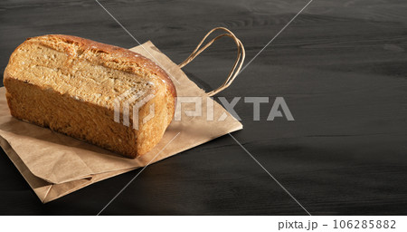 Loaf rustic bread on paper bag on black wooden table is prepared for delivery to buyer. Small business idea, baking and delivery of healthy natural sourdough bread to order. Top view with copy space Loaf rustic bread on paper bag on black wooden table is prepared for delivery to buyer. Small business idea, baking and delivery of healthy natural sourdough bread to order. Top view with copy space 106285882