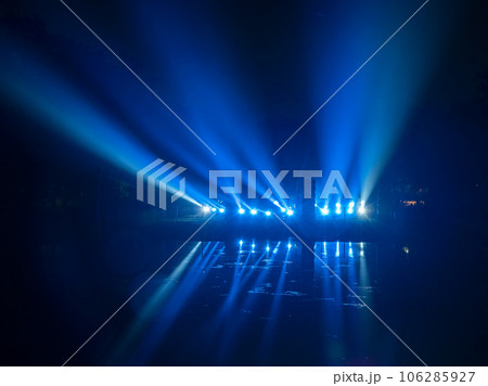 Beautiful laser lights, blue laser in the smoke is reflected from dark lake, an abstract play of light with reflection. 106285927