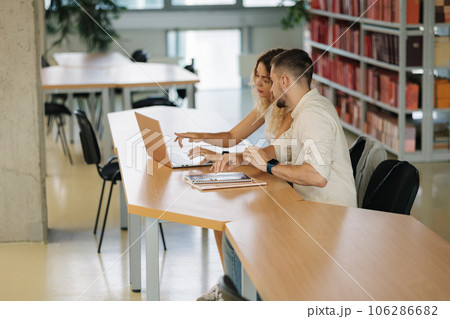 Side view of two classmate of boy and girl study in college library. Girl using laptop. Back view of books 106286682