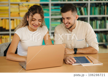 Happy young students of boy and girl preparing in library for exam in university. Two people study. Back view of books 106286721
