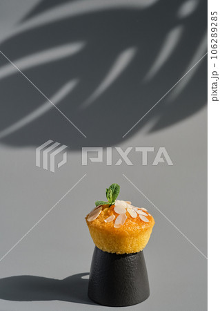 Delicious lemon muffin or cupcake with frosting and almond flakes. Homemade magdalena on gray neutral background, dish serving idea, close-up, selective focus Delicious lemon muffin or cupcake with frosting and almond flakes. Homemade magdalena on gray neutral background, dish serving idea, close-up, selective focus 106289285