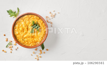 Vegetarian and vegan yellow pea soup with carrots, celery and spices in a clay bowl. Top view of hot soup, focusing on the top of the dish. Layout on concrete white table with copy space Vegetarian and vegan yellow pea soup with carrots, celery and spices in a clay bowl. Top view of hot soup, focusing on the top of the dish. Layout on concrete white table with copy space 106290381