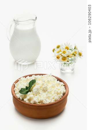 Cottage cheese granulated in earthenware next to a jug of milk. Close-up, selective focus, bright white background. Soft cottage cheese, natural healthy food, complete diet food 106290403