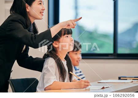 ホワイトボードを見つめる小学生の女の子と若い塾講師 106292056