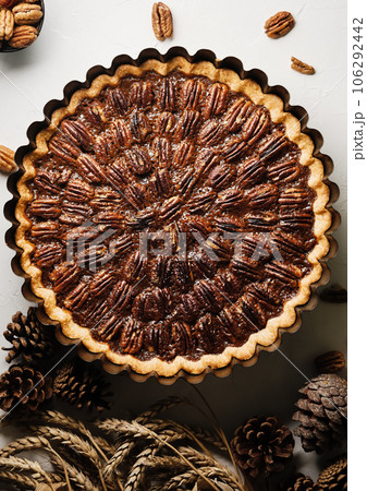 Pecan pie, tart in a baking dish on a white table. Traditional holiday dessert for Thanksgiving or Christmas holidays. View from above. Pecan pie, tart in a baking dish on a white table. Traditional holiday dessert for Thanksgiving or Christmas holidays. View from above. 106292442