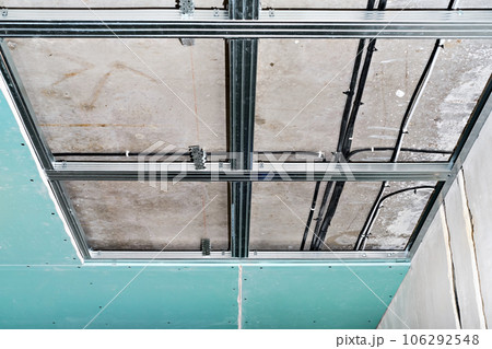 Drywall, installation on a metal frame on the ceiling in a commercial building, office or apartment. A simple and cheap way to renovate a room. Ceiling wiring of the electrical network 106292548