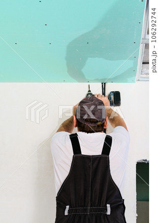 Specialist assembles a suspended ceiling with plasterboard. Assembly process using an electric screwdriver plasterboard to the metal ceiling frame. Simple and affordable renovation of premises 106292744